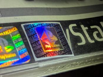 The fake hologram next to a genuine one at an angle, with the fake logo showing only a reddish rainbow sheen.