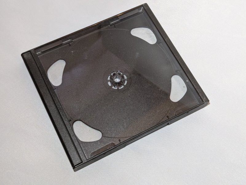 Angled rear view of the mini jewel case showing the black tray through the clear rear leaf, with the four finger access cutouts visible.
