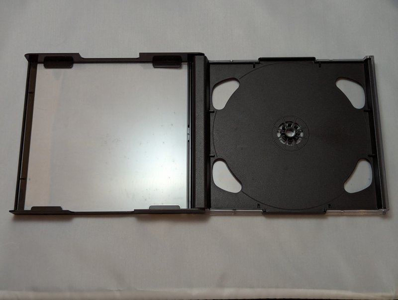 Mini jewel case open flat showing both halves: the black-framed front leaf on the left and the black disc tray with spindle on the right.